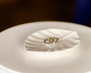 gold wedding rings lie on a white stand in the form of a leaf from a tree