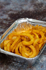 Curly fries in a takeaway foil tray.  On a grunge background