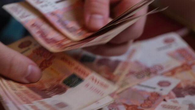 A close-up of the fingers of a hand counting five-thousandth Russian ruble banknotes. Male hands count Russian money 5000 banknotes against the background of a rotating pile of money