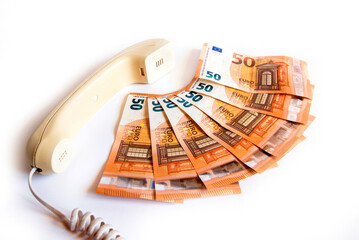 Teléfono tradicional antiguo con cable junto a un conjunto de billetes de 50 euros sobre fondo...