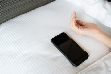 Lazy Asian young woman trying to snooze awaking alarm clock in smartphone.