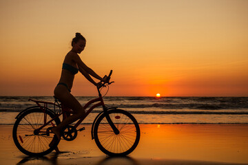Fototapeta na wymiar healthy alone woman ride on bicycle on empty sunset Goa India beach