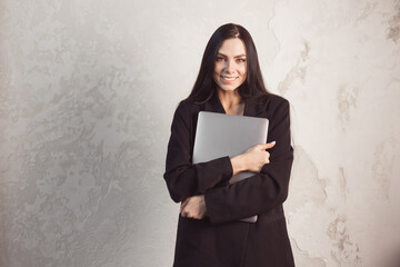 Portrait of glad brunette caucasian woman in black elegant suit hugging computer laptop weared