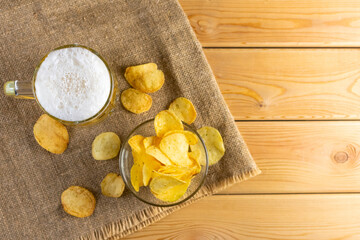 Glass of beer with potato chips on a wooden background. top view