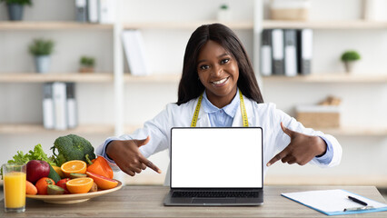 Friendly african american woman dietologist pointing at blank laptop screen, consulting online or...