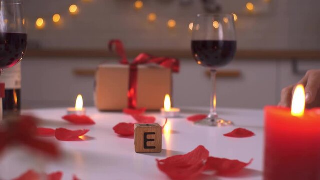 Hands of a couple in love put together the word love. The word love is laid out from cubes. A pair of lovers sits at a table celebrate Valentine's Day. Romantic candles furnishings wine
