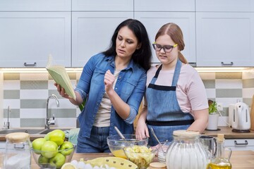 Mother and teenage daughter cooking at home in the kitchen.