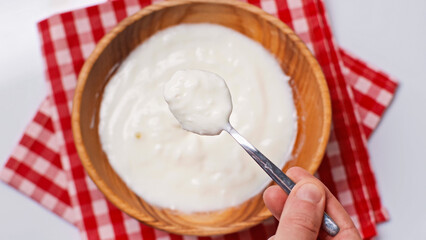top view of man holding spoon with yogurt near blurred bowl on plaid cloth napkin isolated on white