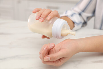 Woman checking temperature of infant formula at table, closeup. Baby milk