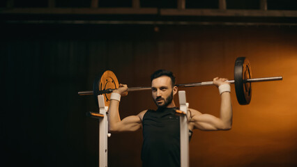 Fototapeta na wymiar Muscular sportsman working out with barbell on dark background