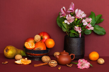 A beautiful still life in warm brown tones with fruits, nuts, a teapot of green tea and a bouquet of pink alstroemeria flowers. Vintage style