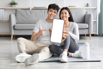 Athletic asian couple exercising from home, showing smartphone, mockup
