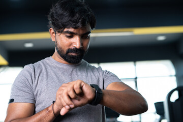 Low angle view of young man monitoring calories or heart rate from smartwatch at gym - concpet of wearable technology, Healthcare and active fitness lifestyle.