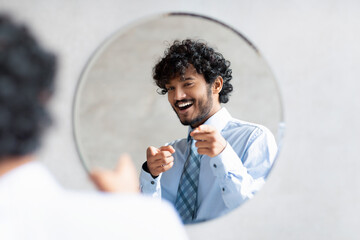 You're handsome. Confident indian businessman pointing at mirror in bathroom with two fingers, wearing shirt and smiling - Powered by Adobe