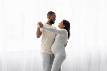 Satisfied cute young african american male and pregnant woman dance on window background, celebrate good news