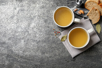 Obraz na płótnie Canvas Hot delicious bouillon in cups on grey table, flat lay. Space for text
