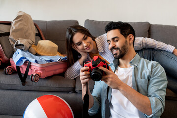 Happy couple packing suitcase and using camera for watching photos in trip. Young spouses preparing for travel