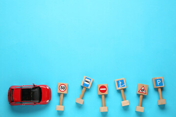 Many different miniature road signs and car on light blue background, flat lay with space for text. Driving school