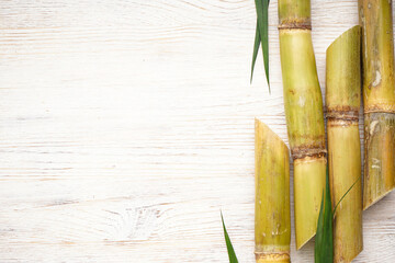 Sugarcane and green leaf close up on rustic white table, space for text. Flat lay.