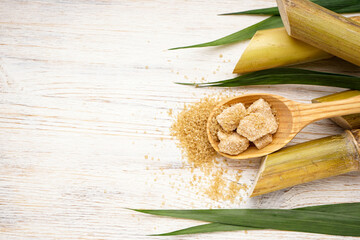 Sugarcane with green leaf and pieces of brown sugar in a wooden spoon on a beige background, space for text. Flat lay.
