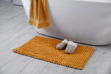 Soft orange mat and slippers on floor near tub in bathroom. Interior design
