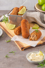 Meat croquets with garlic mayonnaise, lime slices to season and rosemary leaves on wooden table in a kitchen counter top.