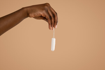 Hand of black woman holding tampon over beige studio background
