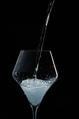 Mineral water is poured into a glass. Black background.