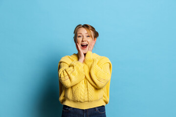 Excited young girl standing with open mouth in surprise isolated on blue background. Concept of wow...