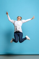 Obraz premium Full-length portrait of excited young girl jumping isolated on blue background. Concept of wow emotions, facial expressions, ad, sales