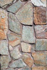Concrete wall trimmed with wild multi-colored stone. Seams are painted with brown paint. Country style. Close-up. Selective focus.