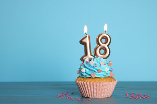 Coming of age party - 18th birthday. Delicious cupcake with number shaped candles on light blue background, space for text