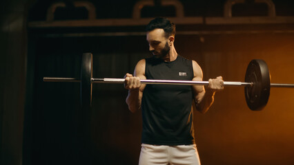 Fototapeta na wymiar Muscular sportsman training with barbell on dark background