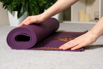 A close-up of a woman's hands roll out a purple mat for yoga or fitness at home