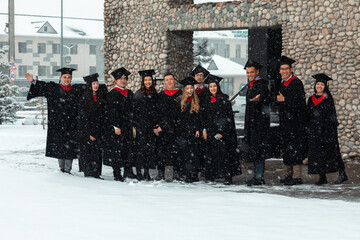 Happy group of graduate students pose together outside during snowfall in gowns