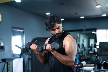 Young man exercsing with dumbbells for biceps at gym - concept of bodybuilding, fitness training...