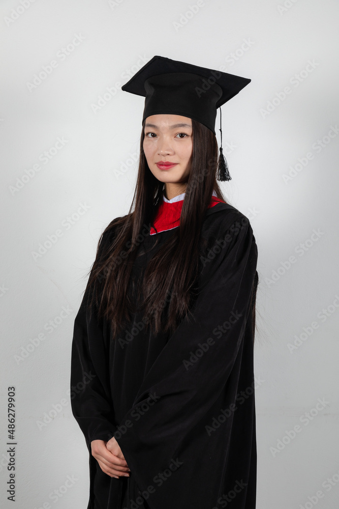 Wall mural Smiling graduate student in mortar board and bachelor gown on white background