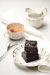 Stack of homemade chocolate brownies on a gray table with cup of tea or coffee, fork, milk jug and napkin. Photo with shallow depth of fields.
