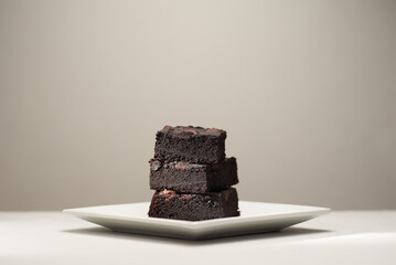 Stack of homemade chocolate brownies on a saucer, gray table and background with place for text. Photo with shallow depth of fields.