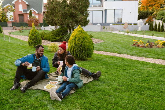 Black family laughing during picnic on blanket at backyard