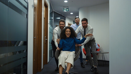 Business group racing chair having fun party in diverse office workplace hallway