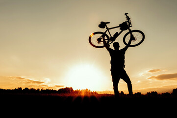 Silhouette of a bicycle over a man's head at sunset.
