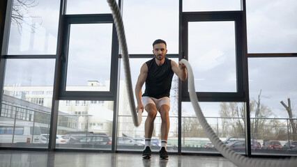 Obraz premium Athletic sportsman training with blurred battle rope in gym