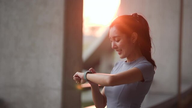 Slim beautiful woman checking sports smart watch in the city at sunrise. Asian female adjusting smart watch before workout outdoor. Exercise in the morning. Healthy and active lifestyle concept.