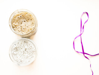 Spa body cosmetics next to purple silk ribbon. Sea salt and body scrub in a glass jar. Natural cosmetics for the body on white background	