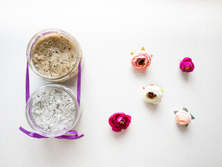 Spa body cosmetics next to the rosebuds. Sea salt and body scrub in a glass jar. Natural cosmetics for the body on white background	