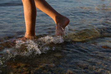 Women legs on the beach. Kid foot in sea water in sunset. Summer holidays and barefoot concept