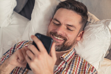 addicted caucasian middle-aged man with facial hair laying in bed and scrolling social media all day long. High quality photo