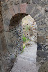 Stone arch and stairways of Khertvisi fortress in Georgia, Caucasus. Ancient weathered medieval grey stone walls and stairs, green grass, doorways and windows