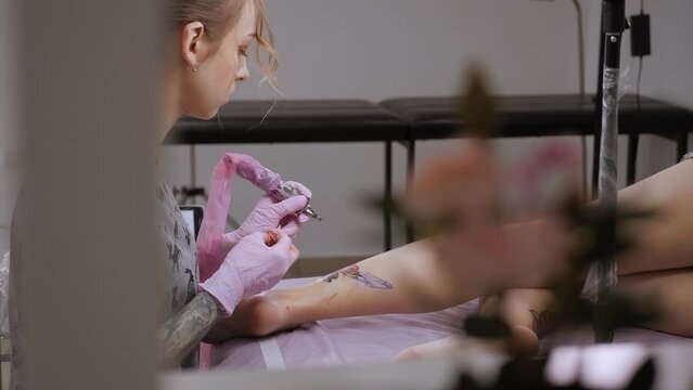 A close-up view of a professional woman tattooist who is tattooing on the leg of a young girl. Hands of a tattooist. Tattooist makes a tattoo. Close-up.